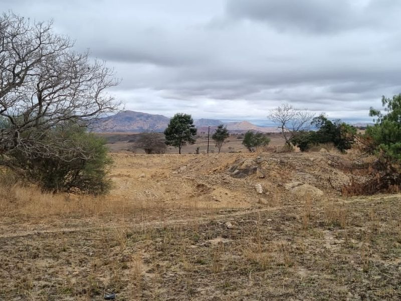 A scenic landscape view of the farm property featuring rolling hills, natural vegetation, and distant mountain ranges under a cloudy sky.