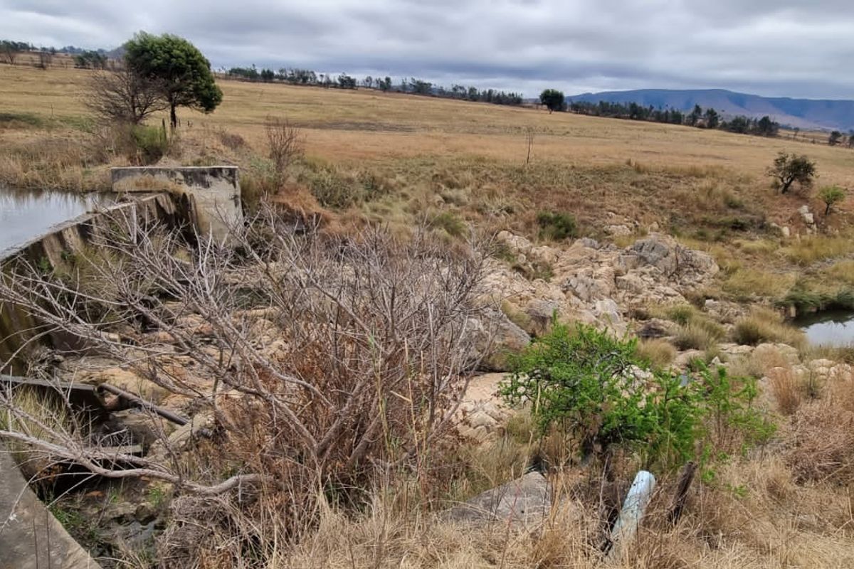 A view of a farm landscape featuring a concrete dam wall and natural rock formations within a rural setting.