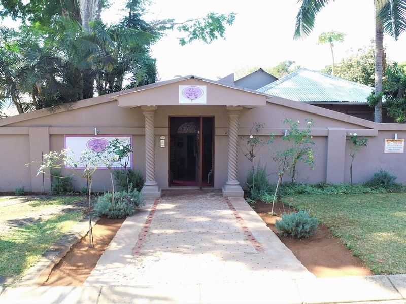 Front elevation of the property featuring a paved walkway leading to a covered entrance with decorative columns and a surrounding boundary wall.
