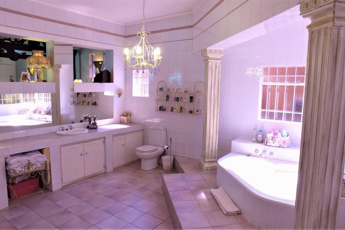 Spacious bathroom featuring a built-in vanity with integrated sink, a raised bathtub area with decorative columns, and full-height wall tiling.