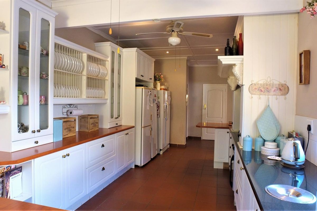 A spacious kitchen featuring white cabinetry, a mix of wooden and stone countertops, tiled flooring, and a ceiling fan.