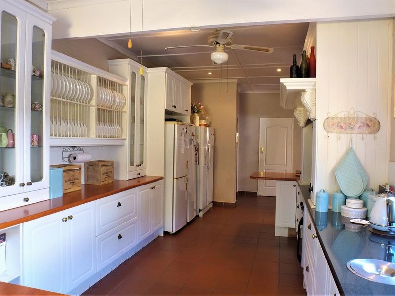 A spacious kitchen featuring white cabinetry, a mix of wooden and stone countertops, tiled flooring, and a ceiling fan.
