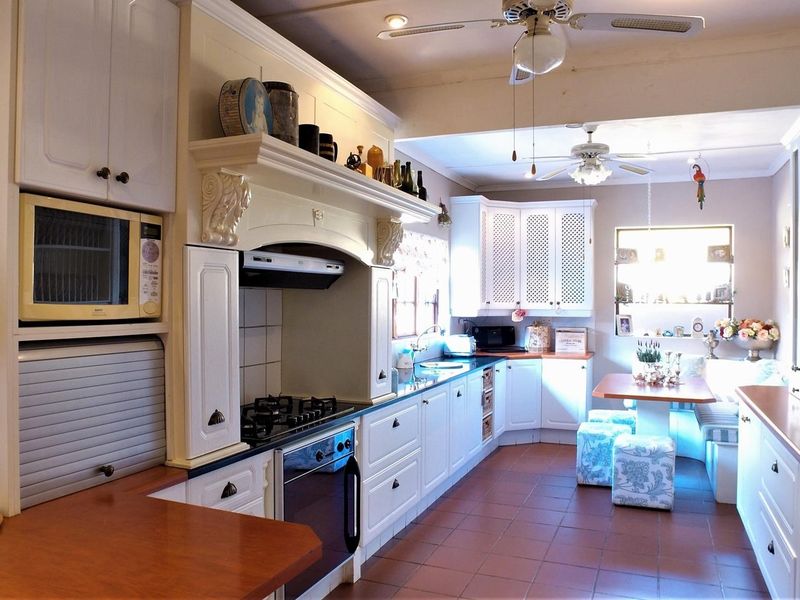 Spacious open-plan kitchen featuring white cabinetry, gas hob, built-in oven, and a cozy integrated breakfast nook with tiled flooring throughout.