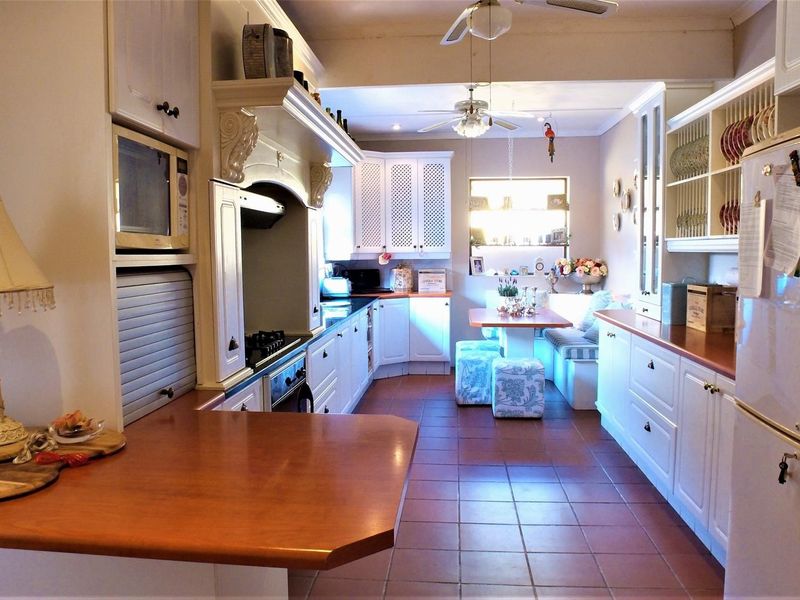 A traditional kitchen featuring white cabinetry, a gas hob with extractor, built-in microwave, and tiled flooring, with an integrated breakfast nook area.