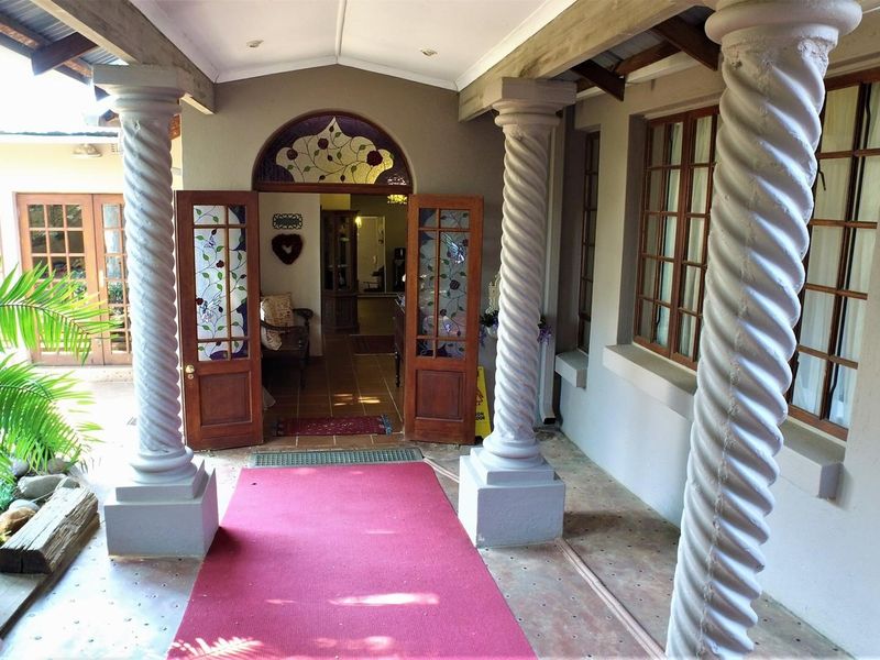 A welcoming covered entrance featuring decorative spiral columns, timber-framed glass doors with stained glass detailing, and tiled flooring.