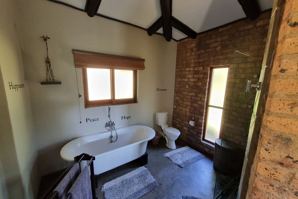 A rustic-style bathroom featuring a freestanding bathtub, a separate glass-enclosed shower, exposed brick feature wall, and vaulted ceilings with exposed timber beams.