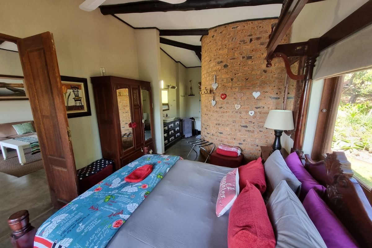 A rustic bedroom featuring a distinctive curved exposed brick feature wall, timber ceiling beams, and an integrated en-suite bathroom area.