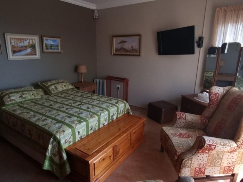 A comfortable bedroom featuring neutral wall tones, carpeted flooring, and large windows with curtains, providing a functional and inviting sleeping space.