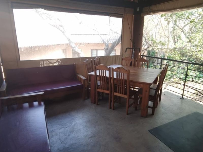 A covered patio area featuring concrete flooring, protective outdoor blinds, and a metal railing overlooking the surrounding garden.