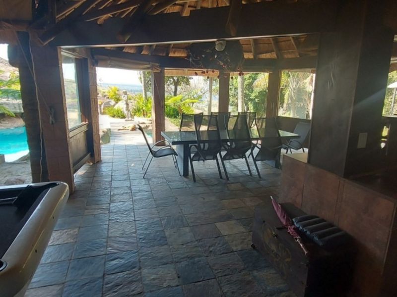 Covered outdoor entertainment area featuring a thatched roof, stone tiled flooring, and direct access to the swimming pool and garden.