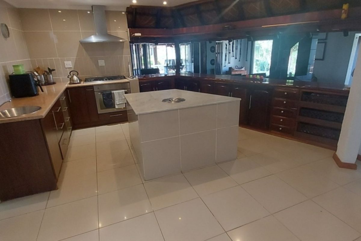 Spacious kitchen featuring dark wood cabinetry, a central island with a prep bowl, tiled flooring, and a stainless steel extractor fan.