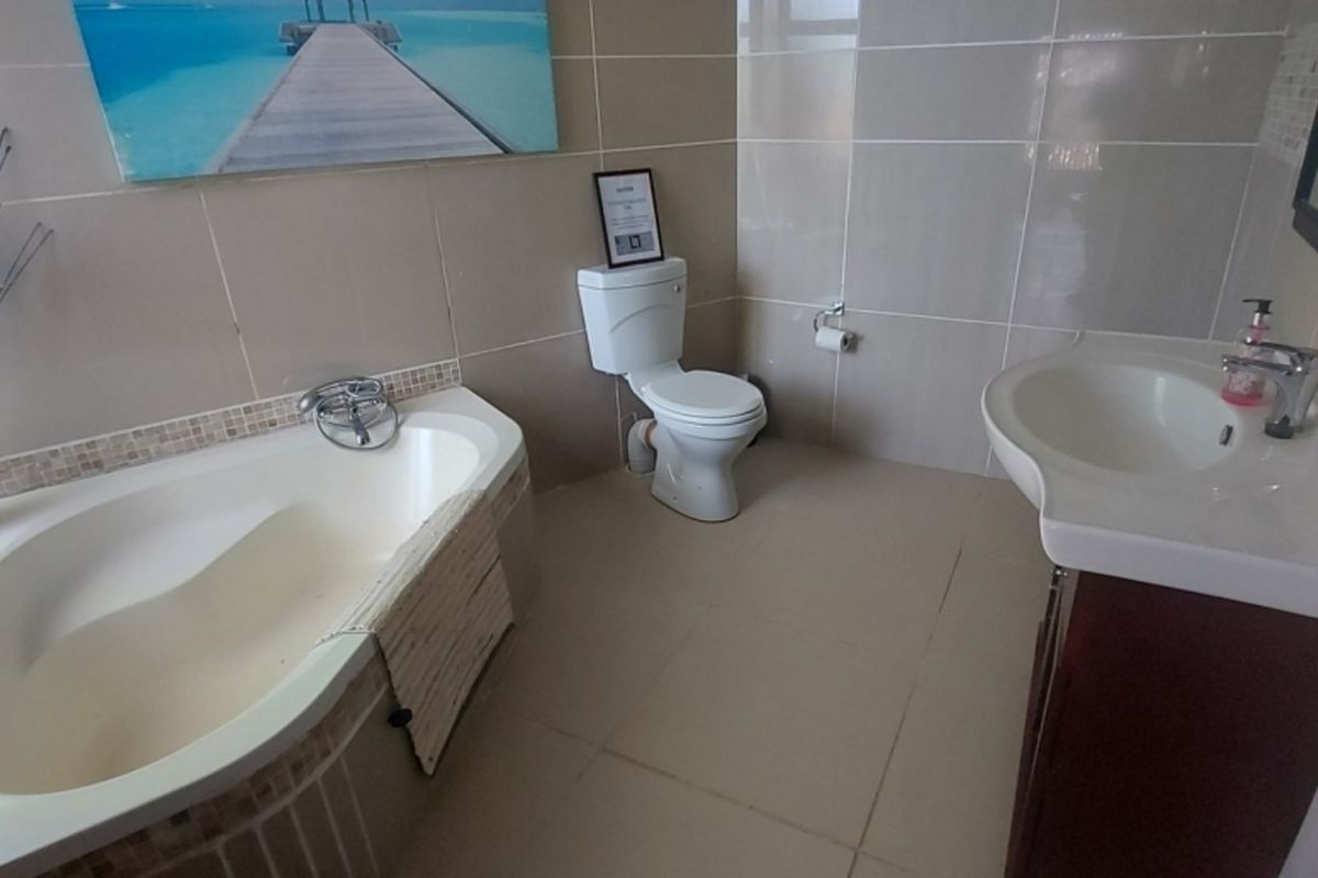 A functional bathroom featuring a built-in bathtub, a standard toilet, and a wall-mounted vanity basin with tiled walls and flooring.