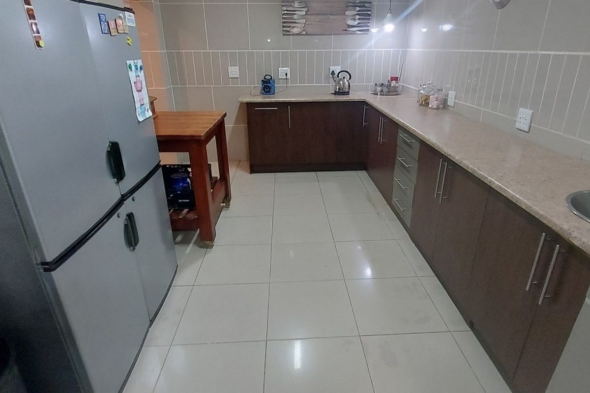 A functional kitchen featuring dark wood cabinetry, light-toned countertops, tiled walls, and tiled flooring.