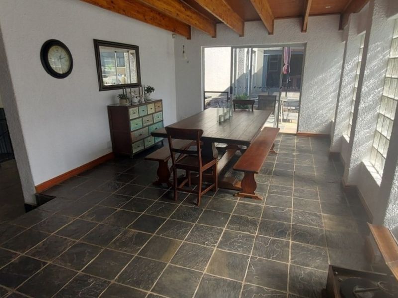 Spacious dining area featuring slate tile flooring, exposed timber ceiling beams, and a glass block feature wall, with direct access to the patio.