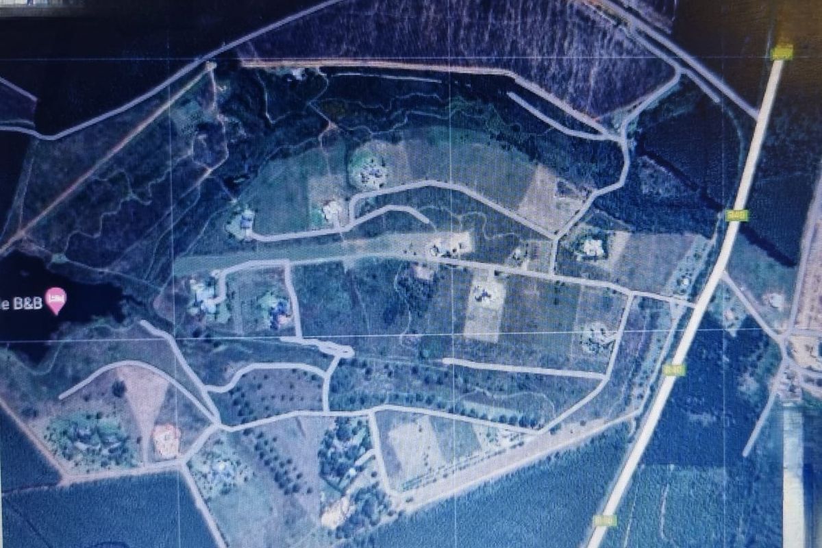 An aerial view of a residential land development showing multiple plots, internal road networks, and surrounding natural landscape.
