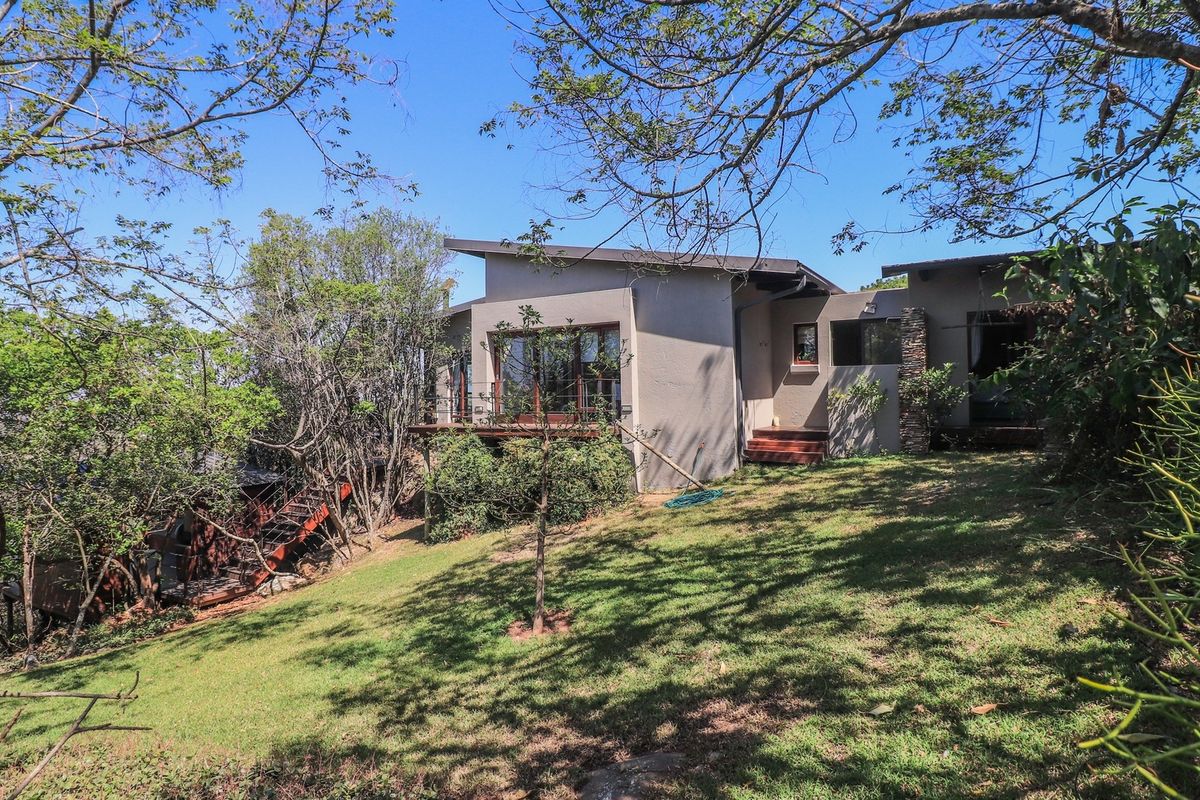 Rear view of the property featuring a modern sloped roof design, timber decking, and stone accents set within a landscaped garden.