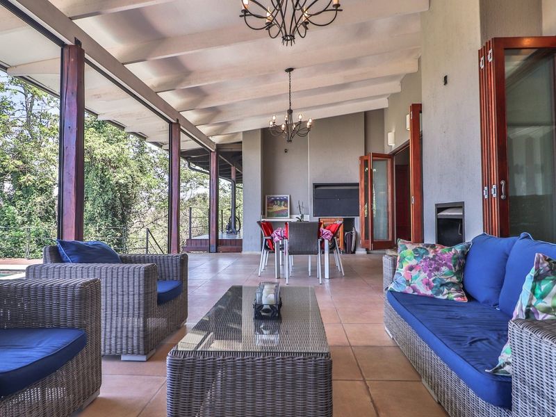 Spacious covered patio featuring an exposed beam ceiling, tiled flooring, built-in braai, and folding timber doors opening to the outdoor area.