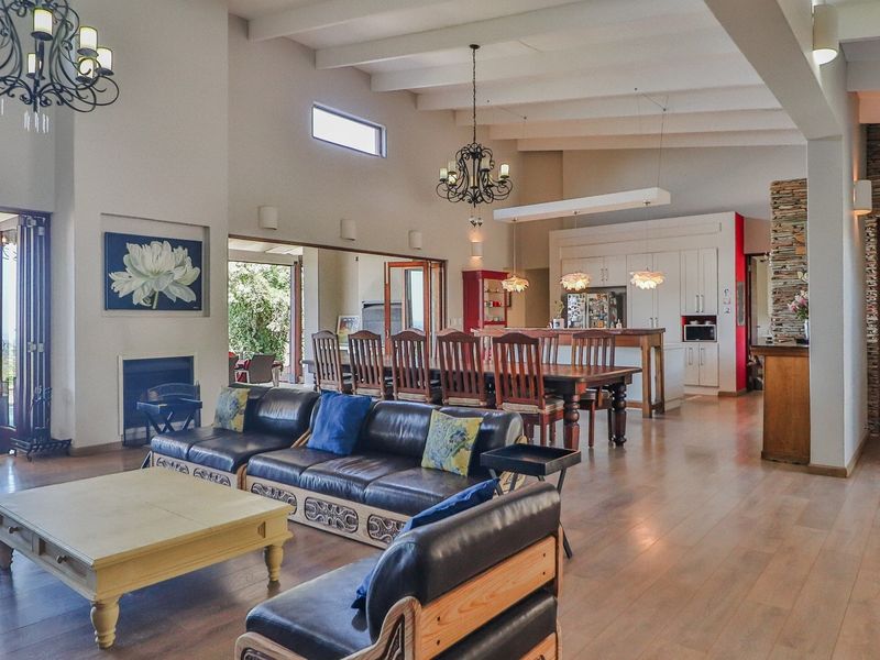 Spacious open-plan living and dining area featuring vaulted ceilings with exposed beams, hardwood floors, a stone feature wall, and a modern kitchen with island.