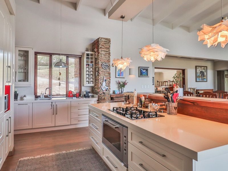 Spacious kitchen featuring a large island with integrated gas hob and oven, shaker-style cabinetry, stone feature pillar, and high exposed beam ceilings.