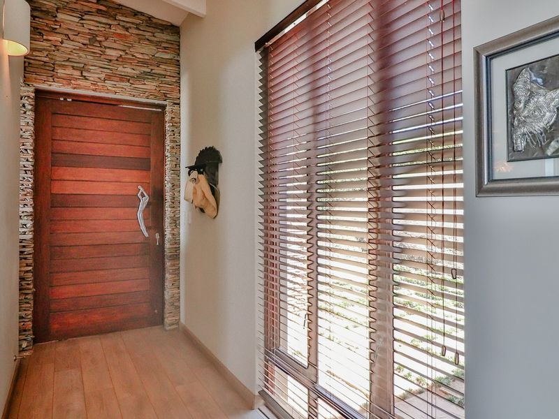 Welcoming entrance hall featuring a solid timber front door, natural stone feature wall, and warm timber flooring with large windows and venetian blinds.