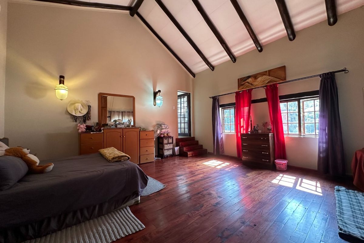 Spacious bedroom featuring high vaulted ceilings with exposed timber beams, polished hardwood flooring, and large windows allowing for ample natural light.