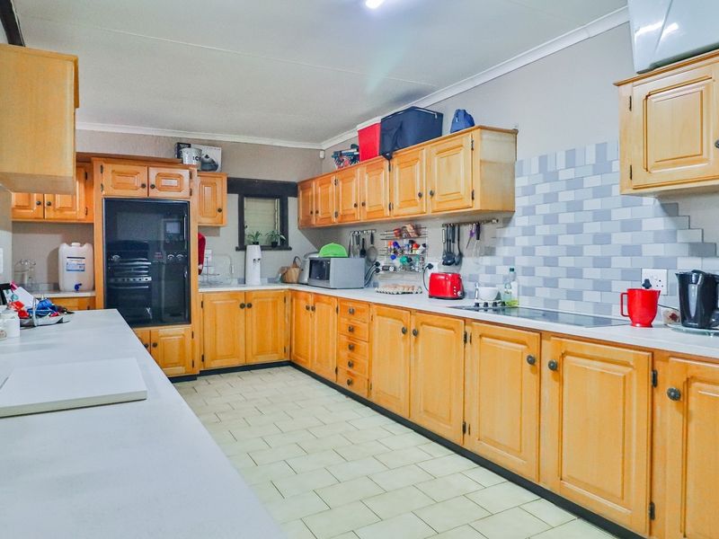 A functional kitchen featuring extensive wooden cabinetry, tiled backsplash, and ample countertop workspace, suitable for a busy farm household.