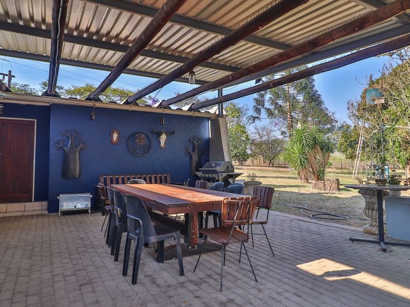 Spacious covered patio area featuring paved flooring, exposed timber beam roofing, and direct access to the expansive farm garden.