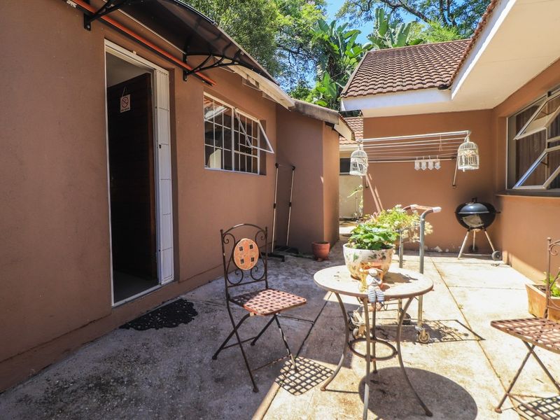 A paved outdoor patio area featuring a covered entrance, security window bars, and a wall-mounted drying rack, suitable for outdoor relaxation.