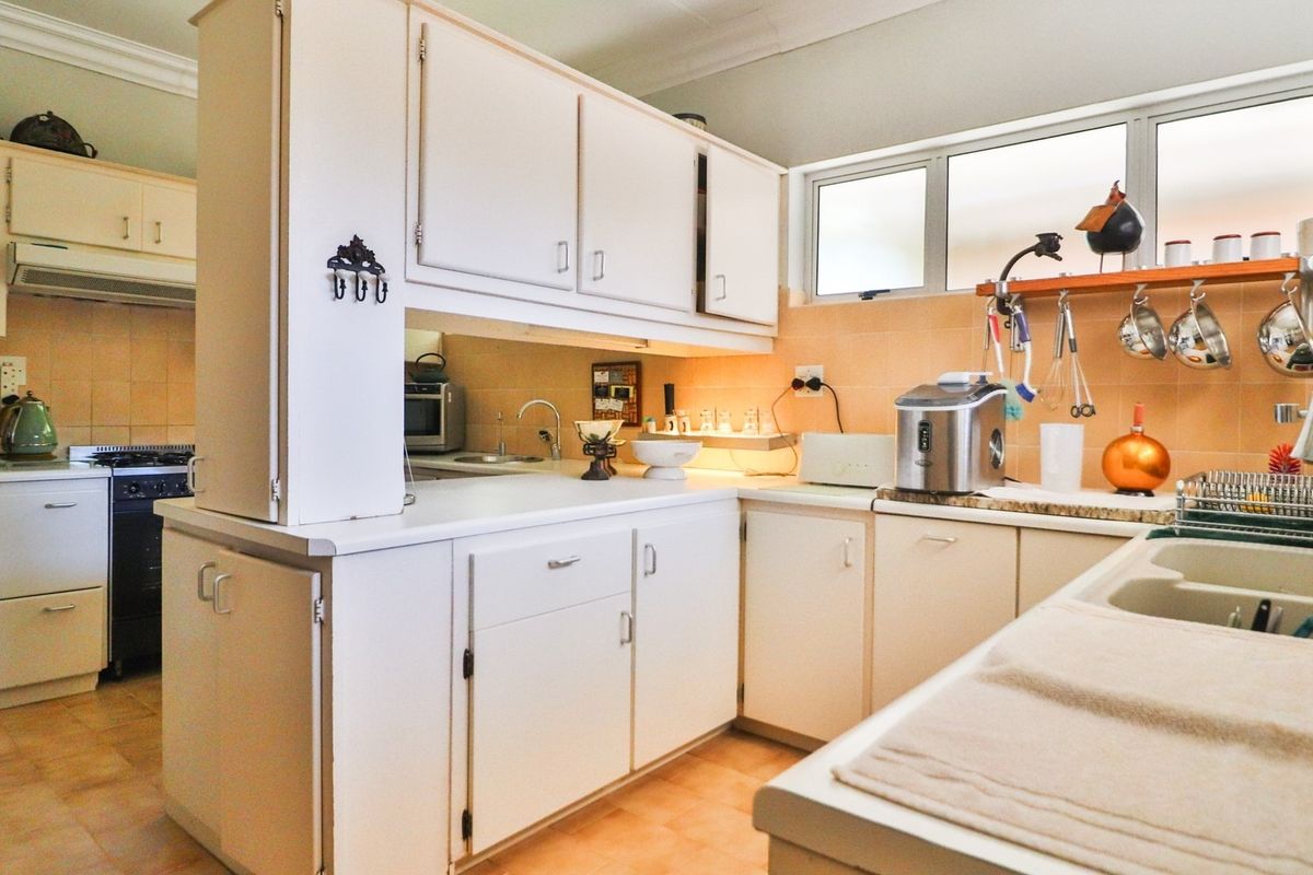 A functional kitchen featuring white cabinetry, tiled splashbacks, a double basin sink, and a built-in stove with an extractor fan.