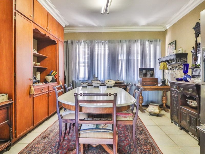 A spacious dining room featuring built-in wooden cabinetry, tiled flooring, and large windows with sheer curtains, providing a functional and traditional dining space.
