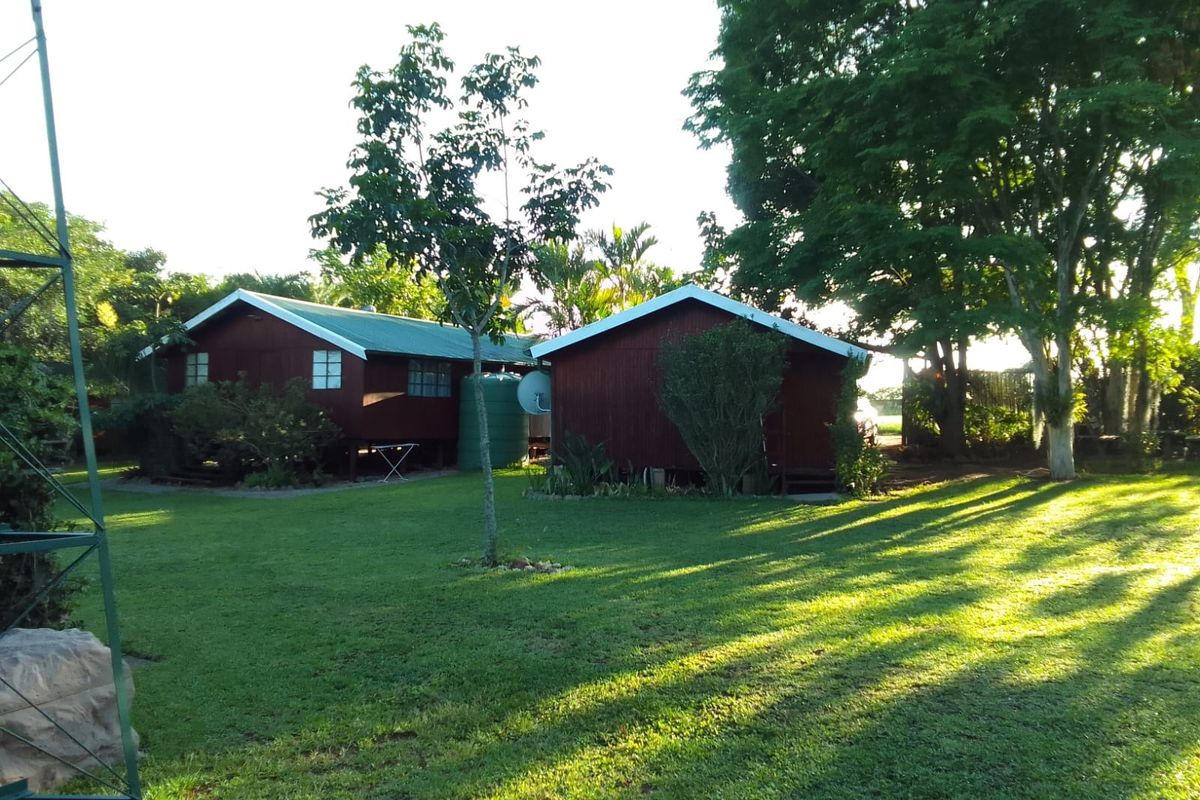 A view of the rear garden featuring two timber-clad structures, a water tank, and a metal windmill frame set within a spacious lawn area.