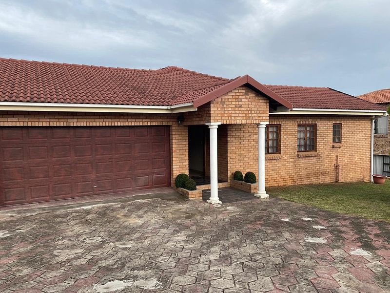 Front view of a single-story brick house featuring a double garage, tiled roof, and a covered entrance with decorative columns.