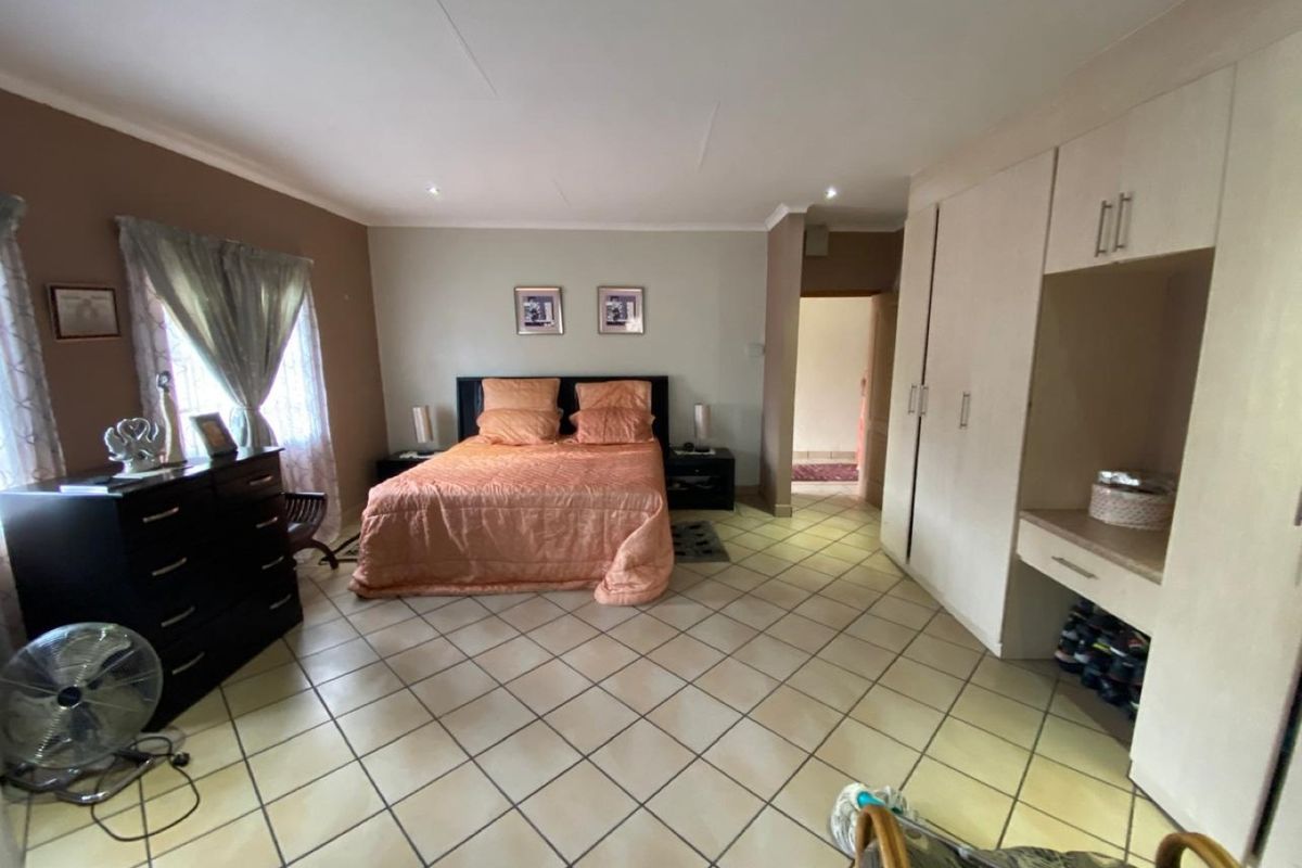 Spacious bedroom featuring tiled flooring, built-in cupboards with integrated vanity space, and recessed downlighting.