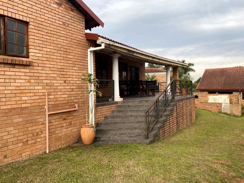 A covered brick patio featuring tiled stairs, metal railings, and structural columns, providing an outdoor entertainment space overlooking the garden.