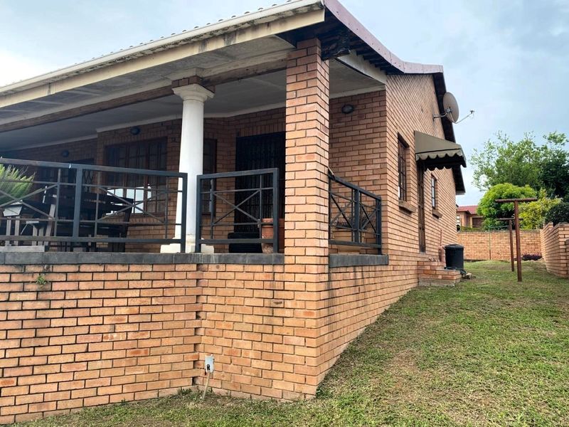 A side view of the house featuring a brick exterior, a covered patio area with metal railings, and a concrete support column.