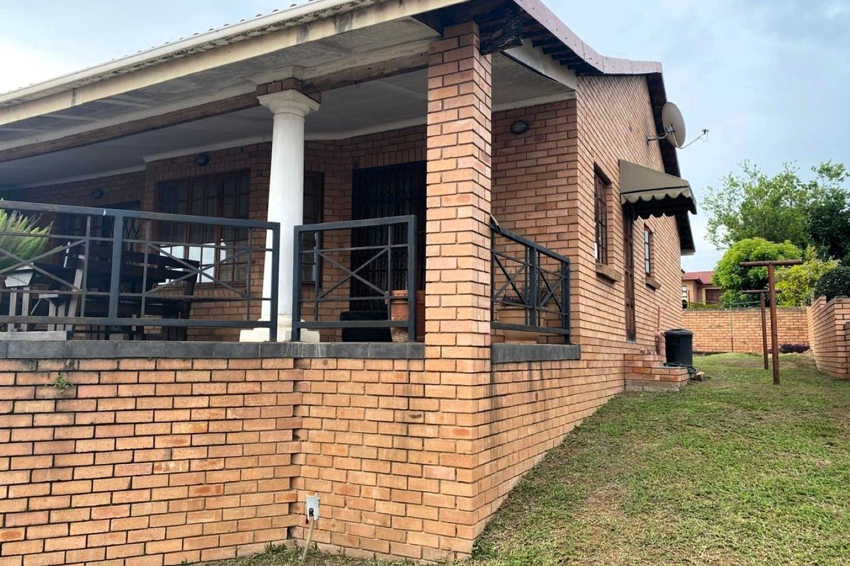A side view of the house featuring a brick exterior, a covered patio area with metal railings, and a concrete support column.