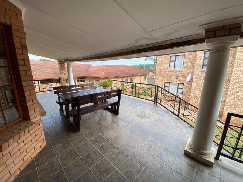 A covered outdoor patio featuring tiled flooring, brick columns, and metal railings, offering a functional space for outdoor dining and relaxation.