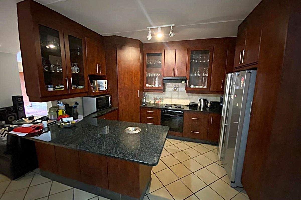 A functional kitchen featuring dark wood cabinetry, granite countertops, built-in oven, hob, and tiled flooring, offering a classic layout with ample storage space.