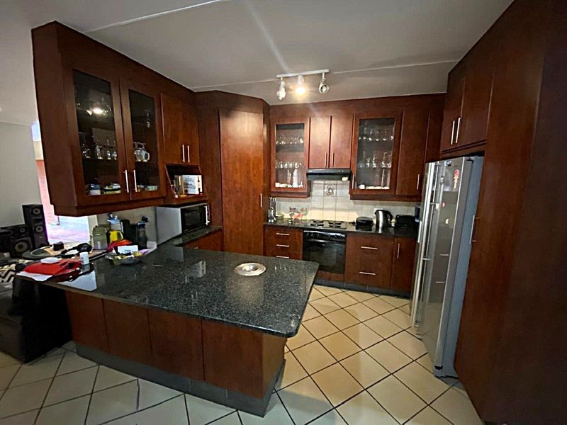 A functional kitchen featuring dark wood cabinetry, granite countertops, built-in oven, hob, and tiled flooring, offering a classic layout with ample storage space.