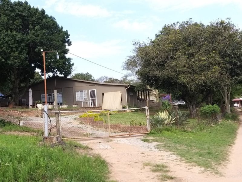 A view of the farm property entrance featuring a gravel driveway, mature trees, and the main dwelling structure set within a rural landscape.