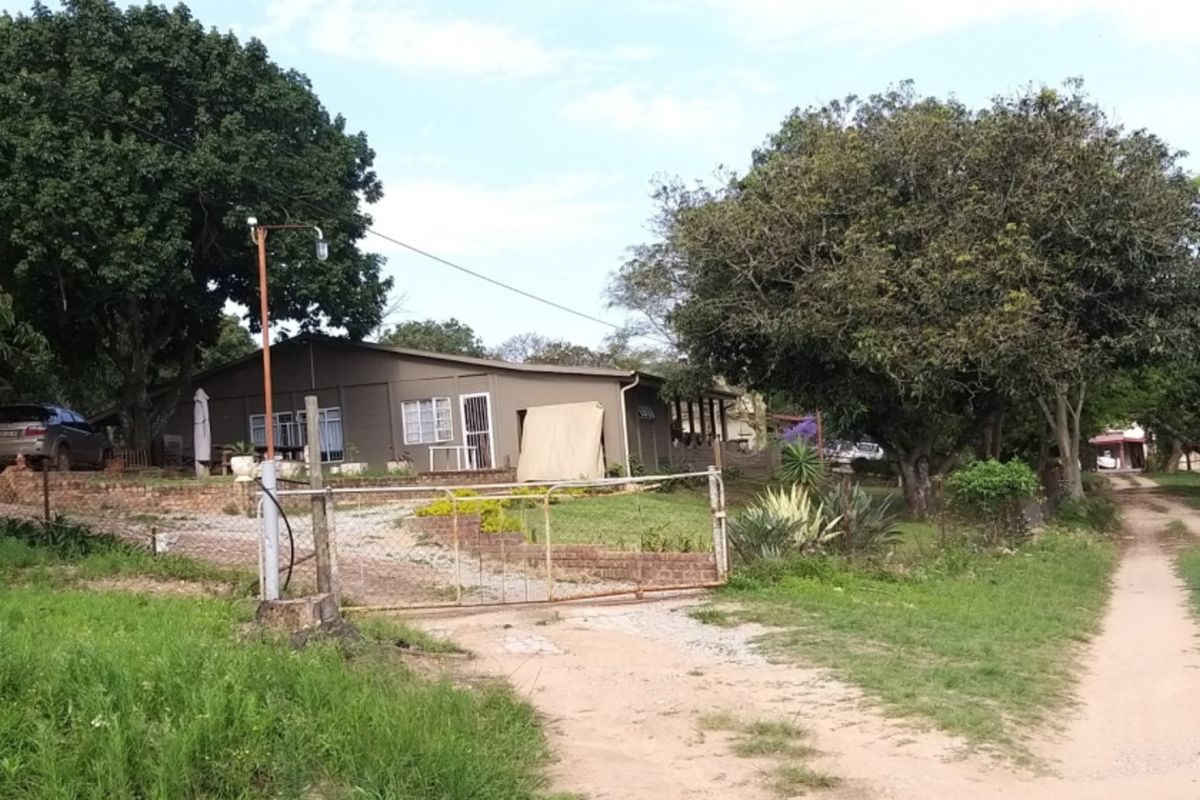 A view of the farm property entrance featuring a gravel driveway, mature trees, and the main dwelling structure set within a rural landscape.