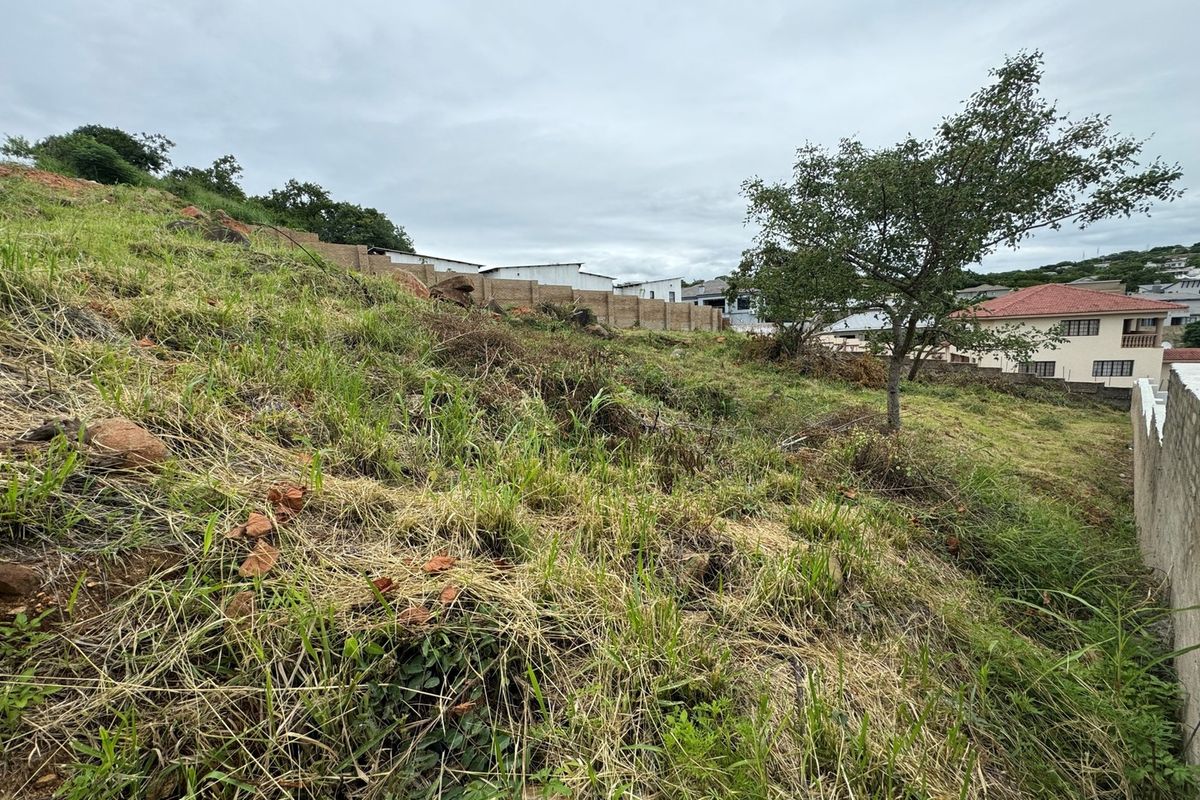 A sloped residential vacant land plot featuring natural grass cover and existing boundary walling, situated in a developed neighborhood.