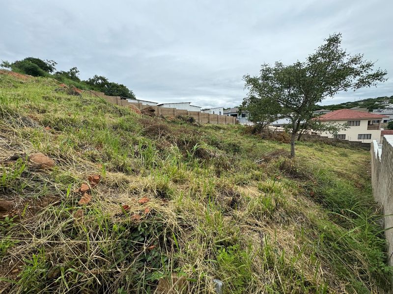 A sloped residential vacant land plot featuring natural grass cover and existing boundary walling, situated in a developed neighborhood.