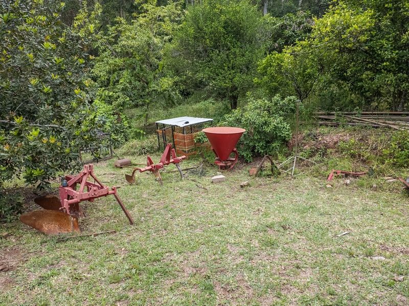 A view of a garden area on the small holding featuring mature trees and lawn, currently used for storage of agricultural equipment.