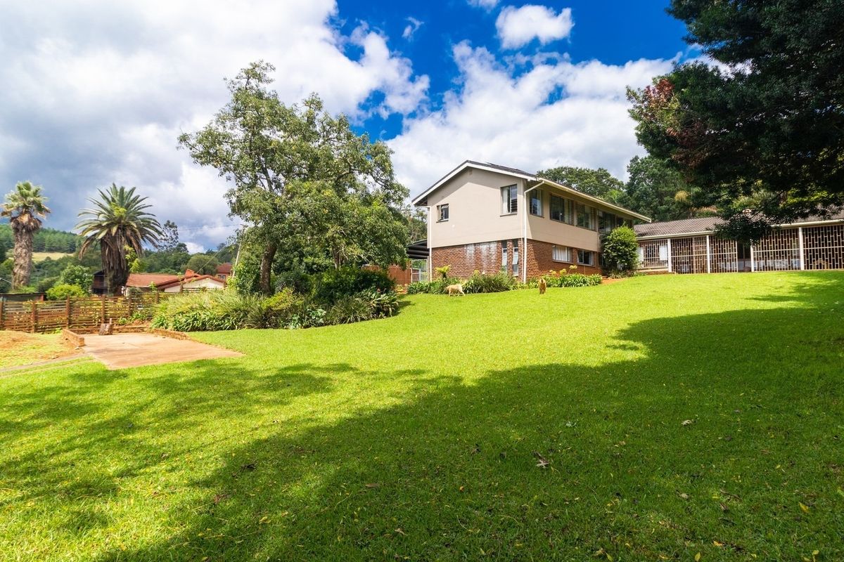 A spacious rear garden featuring a large lawn, mature trees, and a multi-level house with brick and rendered exterior finishes.
