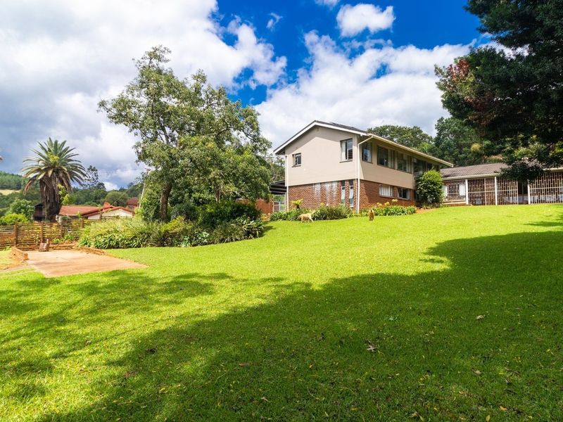 A spacious rear garden featuring a large lawn, mature trees, and a multi-level house with brick and rendered exterior finishes.