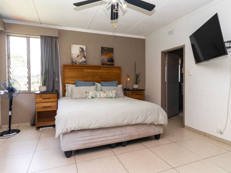 A well-lit bedroom featuring tiled flooring, a ceiling fan, and louver windows, providing a comfortable and functional living space.
