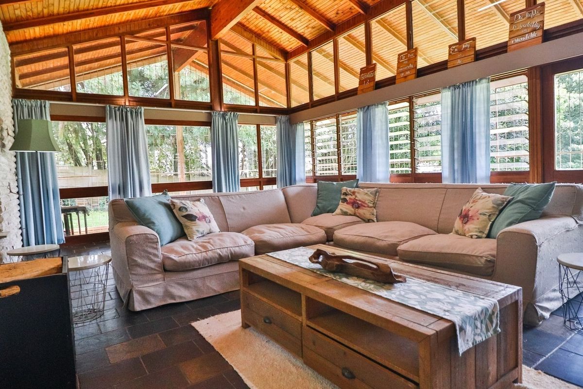 Spacious living room featuring a high exposed timber beam ceiling, stone fireplace, and large windows providing ample natural light and garden views.