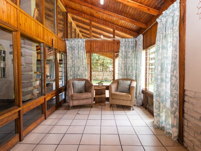 A sunroom or enclosed patio featuring a timber-clad vaulted ceiling, large timber-framed glass walls, and tiled flooring, offering a bright and rustic living space.