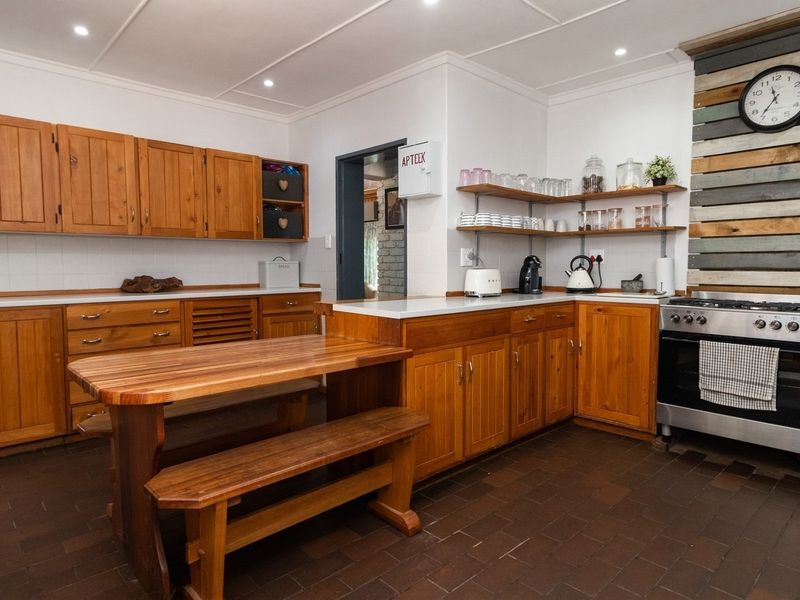 A rustic-style kitchen featuring wooden cabinetry, open shelving, a built-in oven with gas hob, and durable tiled flooring.